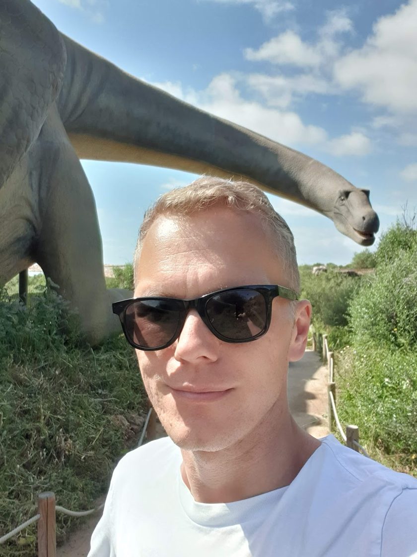 Tobias Zander, portrait with sunglasses and a Brachiosaurus model in the background